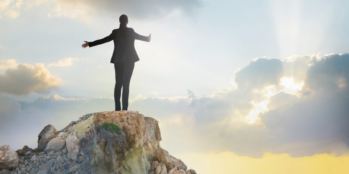 Young woman standing on the top of rock and open hands towards the sun. Success in business concept